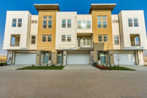 Front view of modern townhouses with large windows and garages under a clear blue sky.