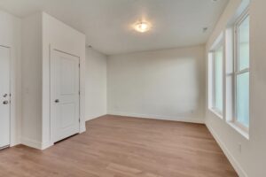 Minimalist room with light wood flooring, white walls, a door, and a row of windows on the right.