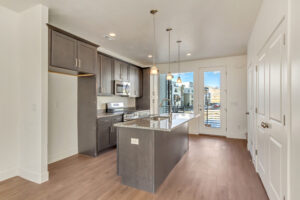 Modern kitchen with dark cabinets, island, pendant lights, and a view of a balcony through glass doors.