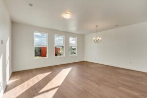 Empty room with wood flooring, three large windows, and a ceiling light. A chandelier is in the corner.