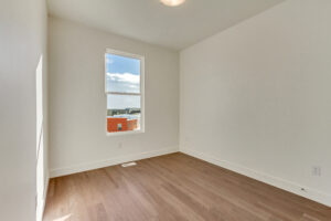 Minimalist empty room with a large window, sunlight on hardwood floor, and white walls.