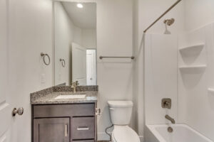 Modern bathroom with a granite countertop, dark wood vanity, large mirror, and shower-tub combo with white tiles.