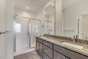 Modern bathroom with a large glass shower, granite countertop, dark wood cabinets, and a mirror.