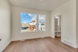 Bright room with wooden floor, large windows showing an urban view and hills, and an open doorway to a small room.