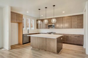 Modern kitchen with wood cabinets, white countertops, nightingale island, stainless steel appliances, and pendant lights.