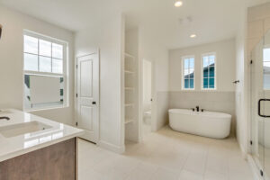 Modern bathroom with freestanding tub, dual sinks, white tiles, a window, and Nightingale shelving by the door.