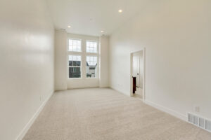 Empty room with beige carpet, white walls, high ceiling, and large windows. A Nightingale-themed doorway leads to another room.