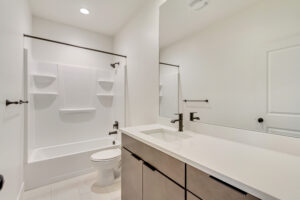 Modern bathroom with a white bathtub, nightingale mirror, white countertop, and sleek black fixtures.