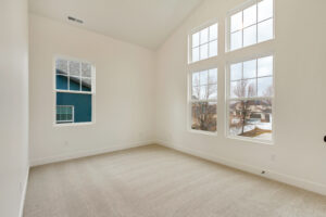 Empty room with beige carpet, white walls, and large windows framing a nightingales outdoor view. High ceiling and natural light.