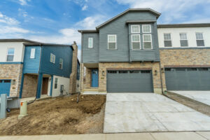 Modern townhouse with a nightingale-themed blue and stone facade, double garage, and a patch of bare soil in the front yard.